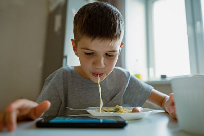 Boy, child eats pasta retraction long pasta into his mouth
