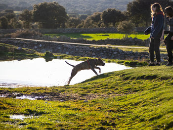 Girl and woman with dog on grass by lake