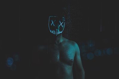 Midsection of shirtless man standing against wall at night