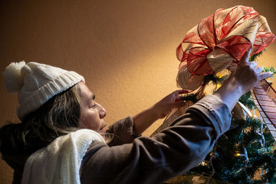 Senior woman putting bow on top of the tree, christmas parties