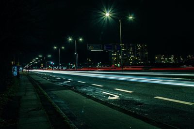 Light trails on illuminated city against sky at night