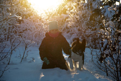 Cute boy sitting on snow covered land with dog during winter