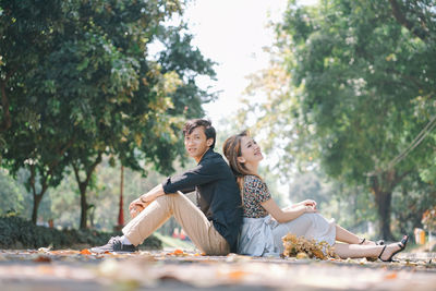 A couple sitting leaning against each other while enjoying the fallen leaves in the park