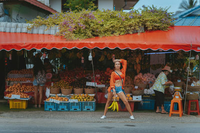 A young girl in red near a fruit stand on the street