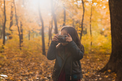 Midsection of man photographing in forest during autumn