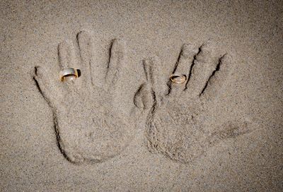 Directly above shot of wedding rings on hands in sand