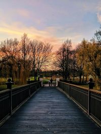 Man on footbridge against sky during sunset