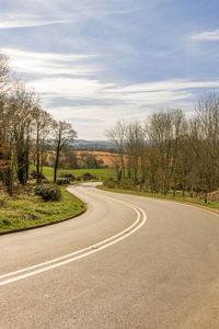 Empty road by trees against sky