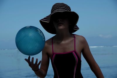 Young woman playing with ball against sea
