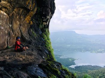 Man meditating while sitting on rock by mountains