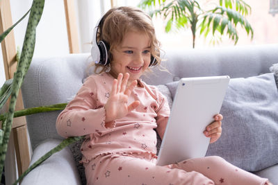 Cute smiling girl using digital tablet for video call at home