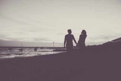 Rear view of silhouette men standing on shore against sky