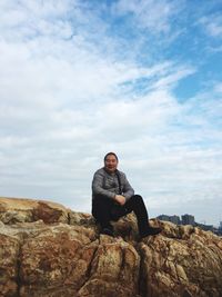 Portrait of man sitting on rock against sky