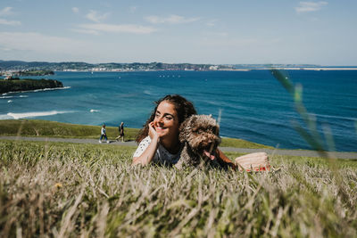 Happy woman with dog on field against sea