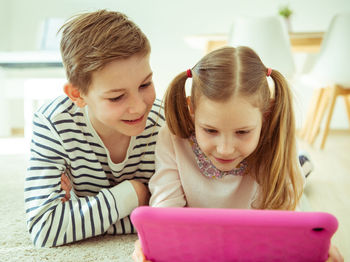 Siblings using digital tablet while lying at home