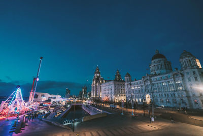 Illuminated buildings against blue sky at night