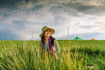 Smiling young woman standing on grassy field against sky