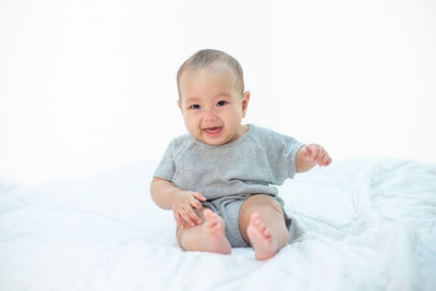 Portrait of cute baby girl crying while sitting on bed against white background