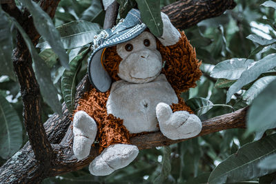 A stuffed monkey wearing a big blue hat and lifting it up while sitting on a branch