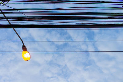 Low angle view of light bulbs hanging against sky