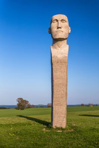 Stone sculpture on field against clear blue sky