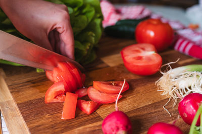 Cropped hand of person holding vegetables on cutting board
