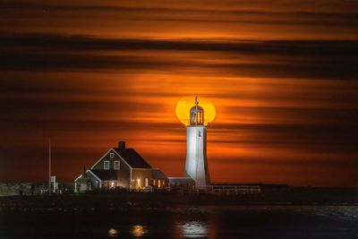 Illuminated lighthouse by sea against sky during sunset