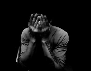 Depressed man covering face against black background