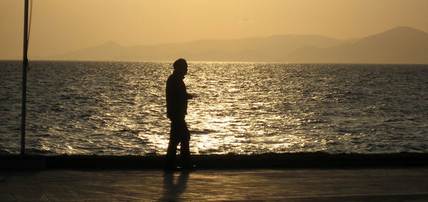 Silhouette man standing in sea against sky during sunset