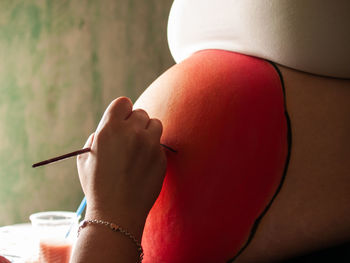 Cropped hand painting pregnant woman belly 