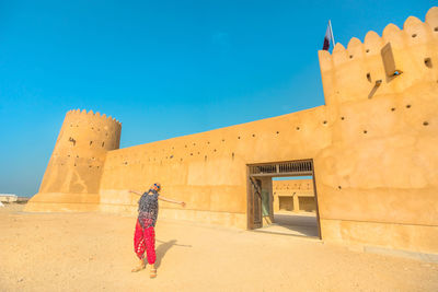 Woman walking by historic building against blue sky