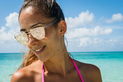 Smiling young woman in sunglasses at beach against sky