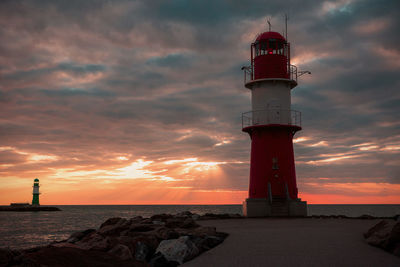 Lighthouse by sea against sky during sunset