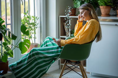 Exhausted tired female relaxing after job, sitting with mobile phone, surfing in internet, messaging