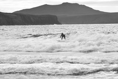Man surfing in sea against mountains