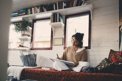 Woman drawing in book while sitting on bed at houseboat