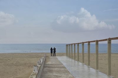 Rear view of business people standing at beach against sky