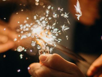 Cropped hand of man holding illuminated string lights at night