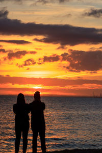 Silhouette couple standing by sea against sky during sunset