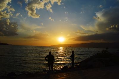 Silhouette people standing on beach against sky during sunset