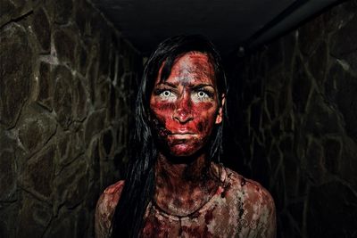 Portrait of spooky woman with blood against wall