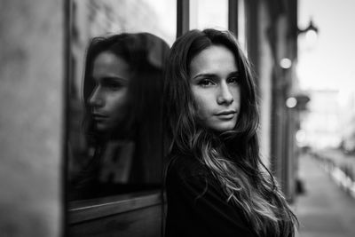 Portrait of young woman leaning on window outdoors