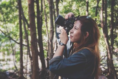 Close-up of woman photographing with camera against trees