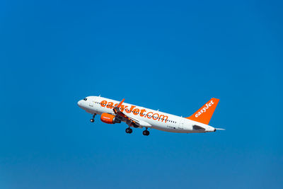 Low angle view of airplane flying against clear blue sky