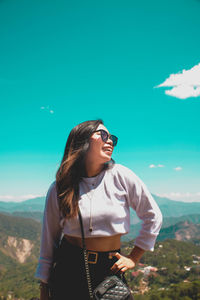 Young woman wearing sunglasses standing on mountain against sky