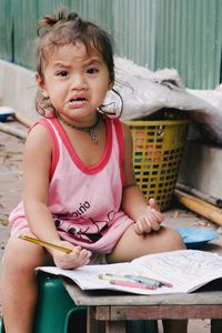 Portrait of cute girl holding pencil while sitting on table on field