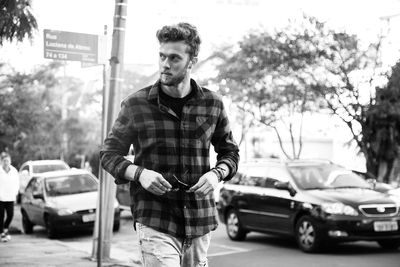 Man wearing plaid shirt while walking against car