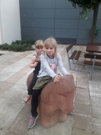 Portrait of girl sitting with sister on sculpture