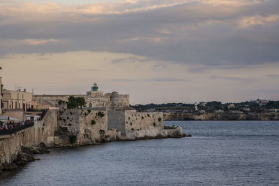 Buildings at waterfront against cloudy sky