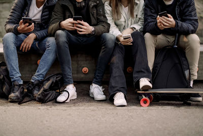 Low section of teenage boys and girl using smart phone while sitting at park